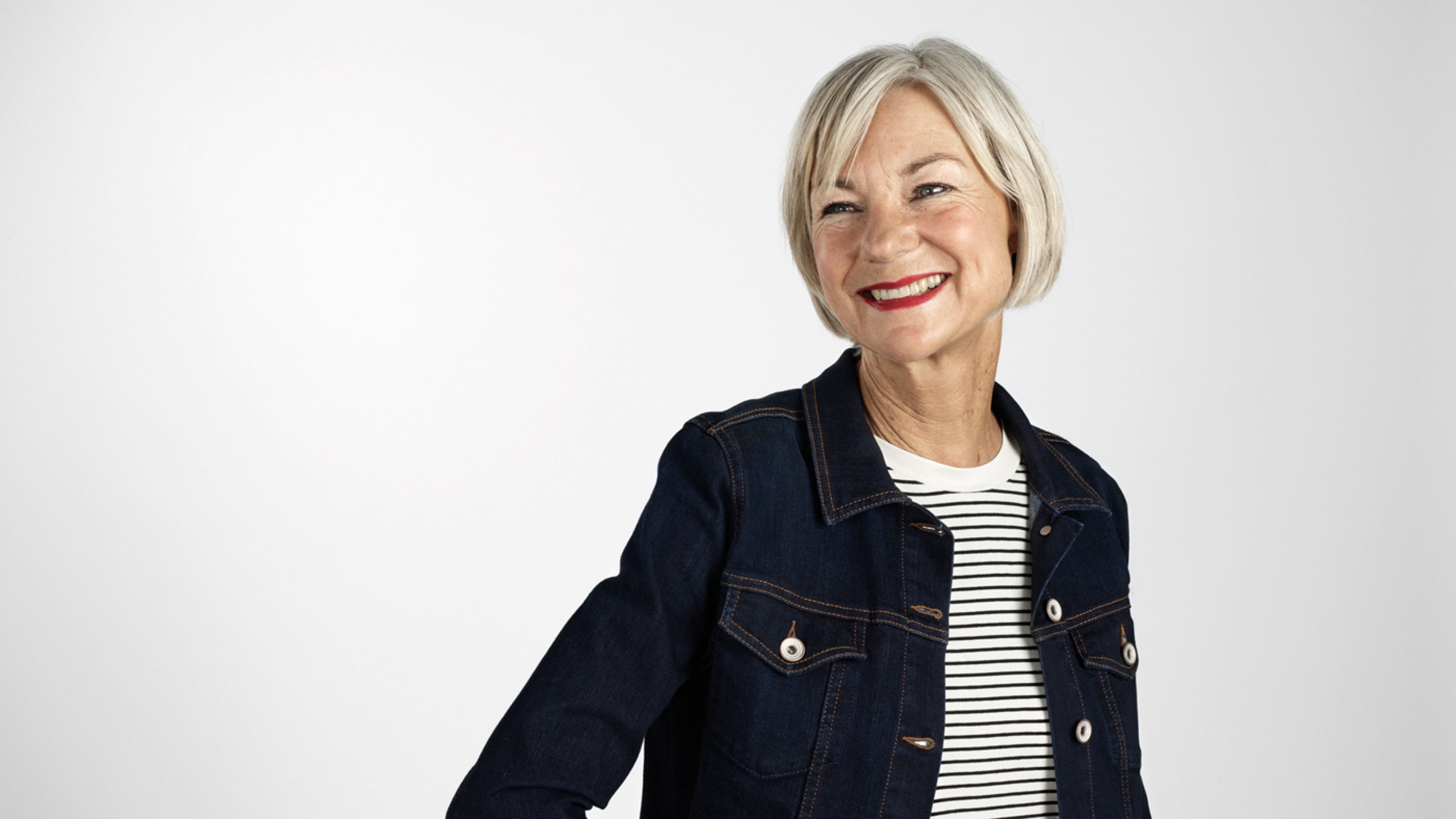 Une personne âgée souriante avec une veste en jean noir.