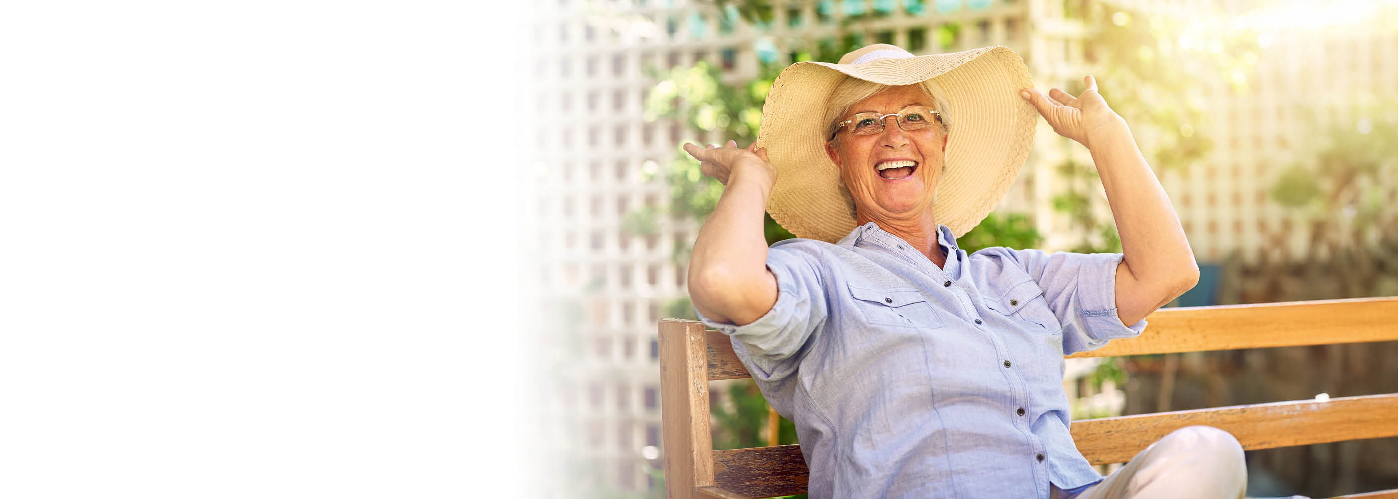 Une dame âgée avec un chapeau est assise sur un banc en été.