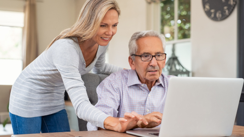 Eine Frau hilft einem älteren Herrn am Laptop